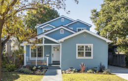 Blue two-story house with white trim, a front porch, and surrounding trees.