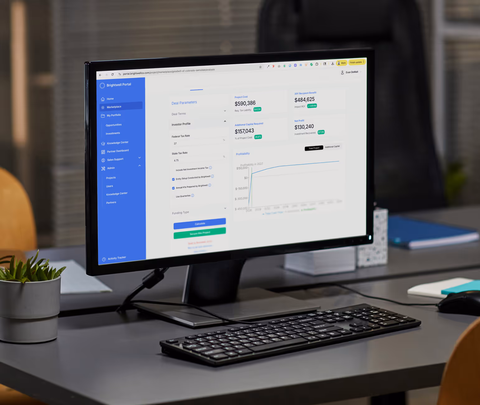Desktop computer monitor on office desk displaying a financial dashboard with deal parameters, project cost, ROI, and profitability chart.