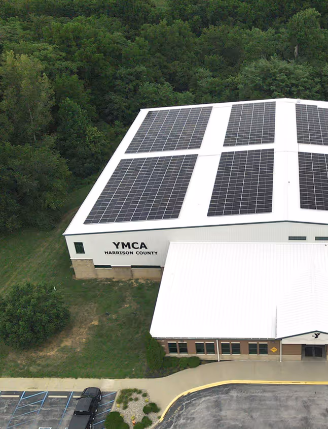 Aerial view of the YMCA Harrison County building with solar panels on the roof and surrounded by trees.