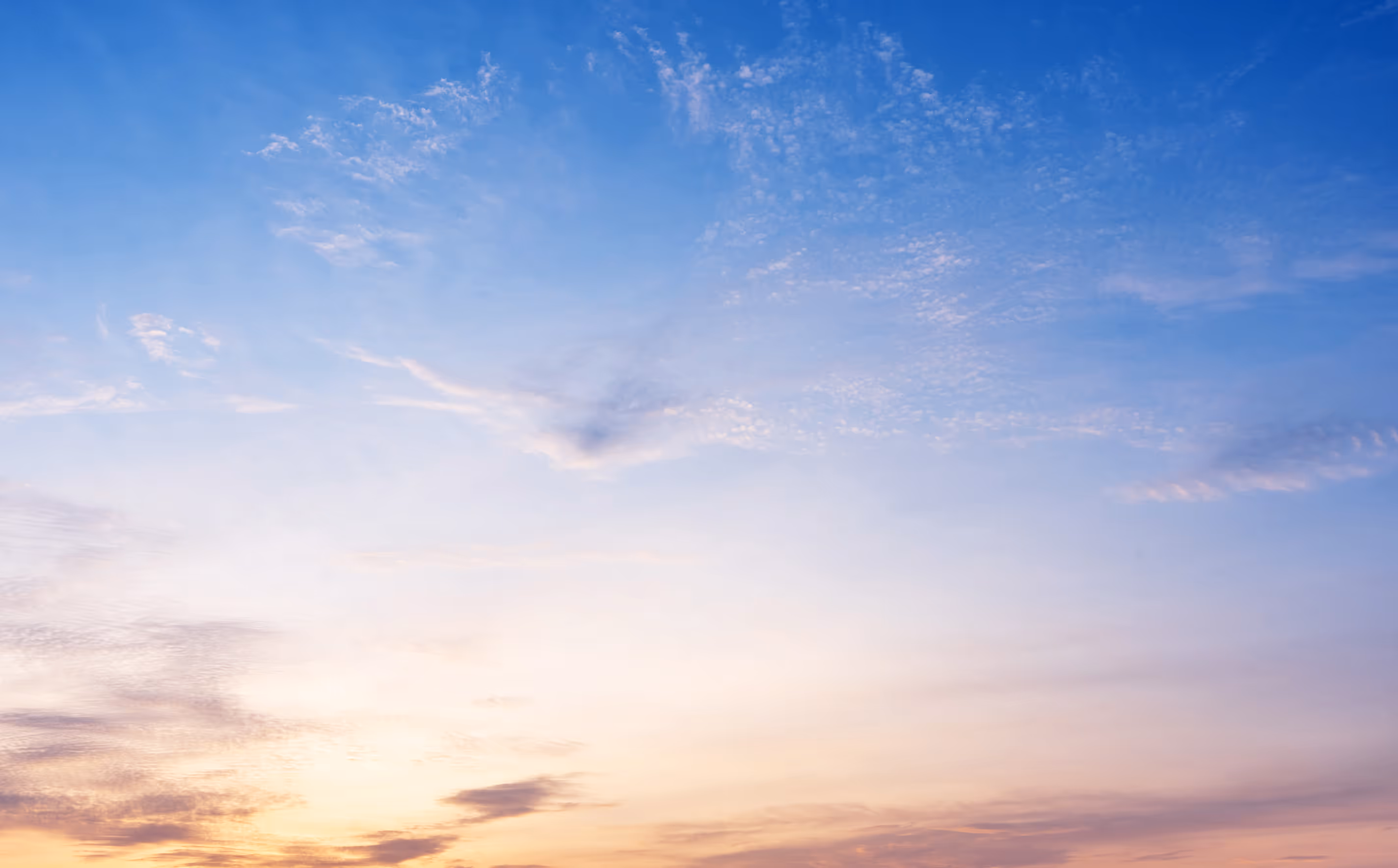 Sky at sunrise with soft pastel colors and scattered wispy clouds.