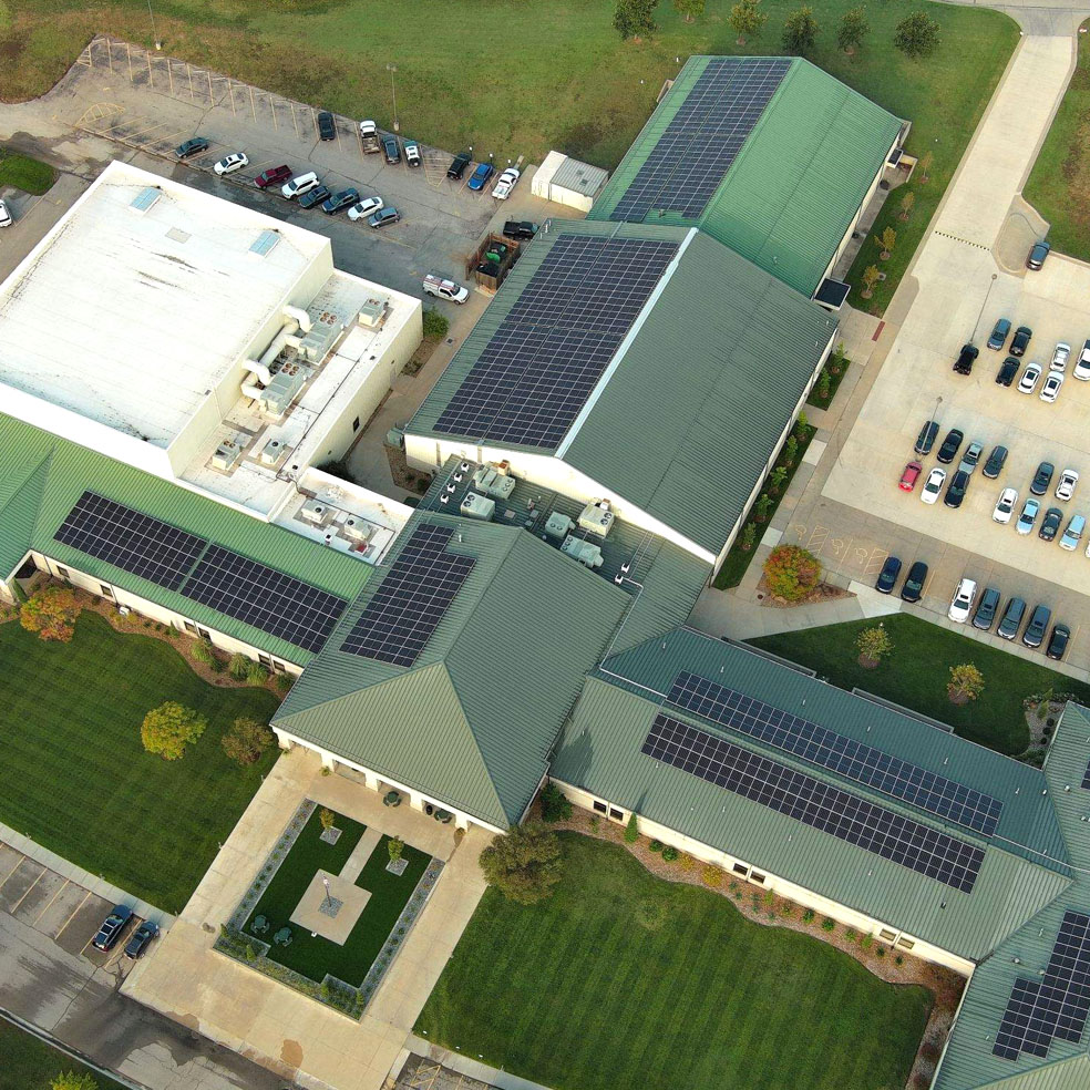 Aerial view of a large commercial building complex with multiple green roofs equipped with solar panels and surrounding parking lots.