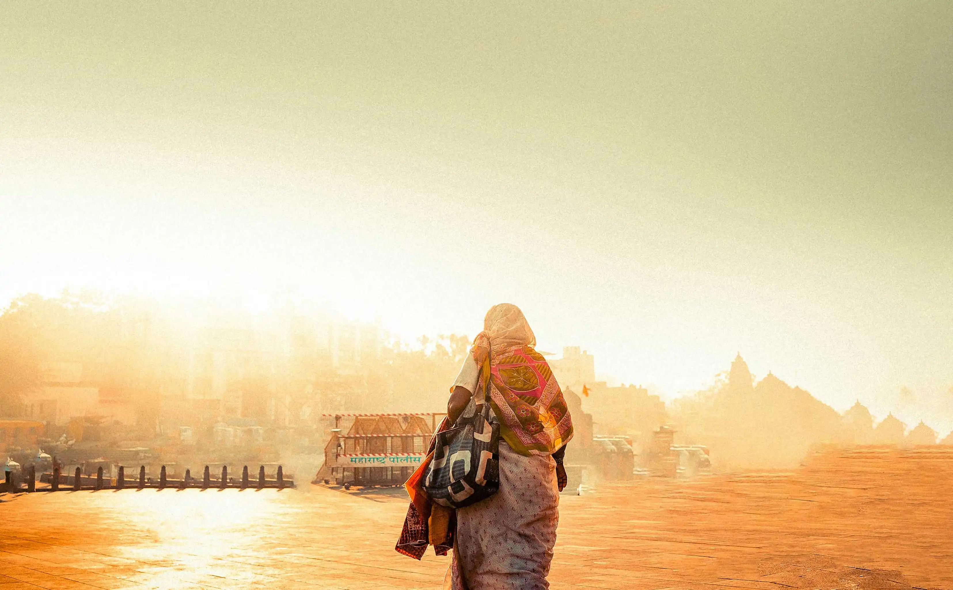 Woman in traditional Indian sari walking on a sunlit street with hazy buildings in the background.