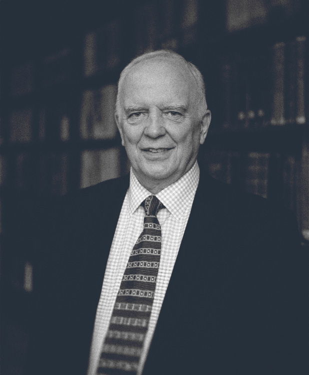 Ian Hamilton in a suit, checkered shirt, and patterned tie with bookshelves in the background.