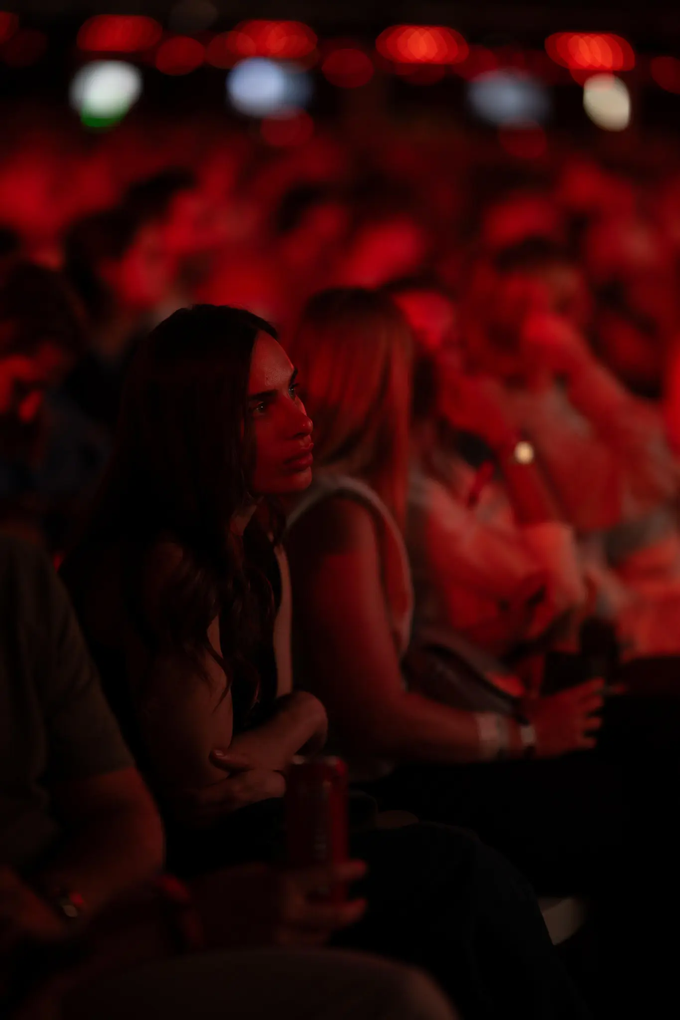 Woman with long dark hair sitting among a crowd bathed in red light, attentively watching something at the Love Tomorrow Summit