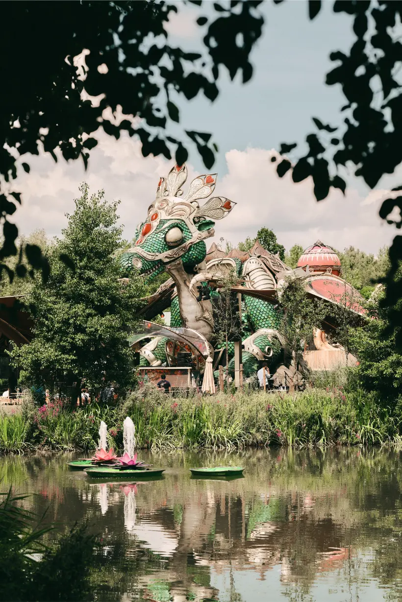 Large green and white dragon sculpture with red accents framed by foliage, reflecting in a pond with floating fountains and lily pads at the Love Tomorrow Summit