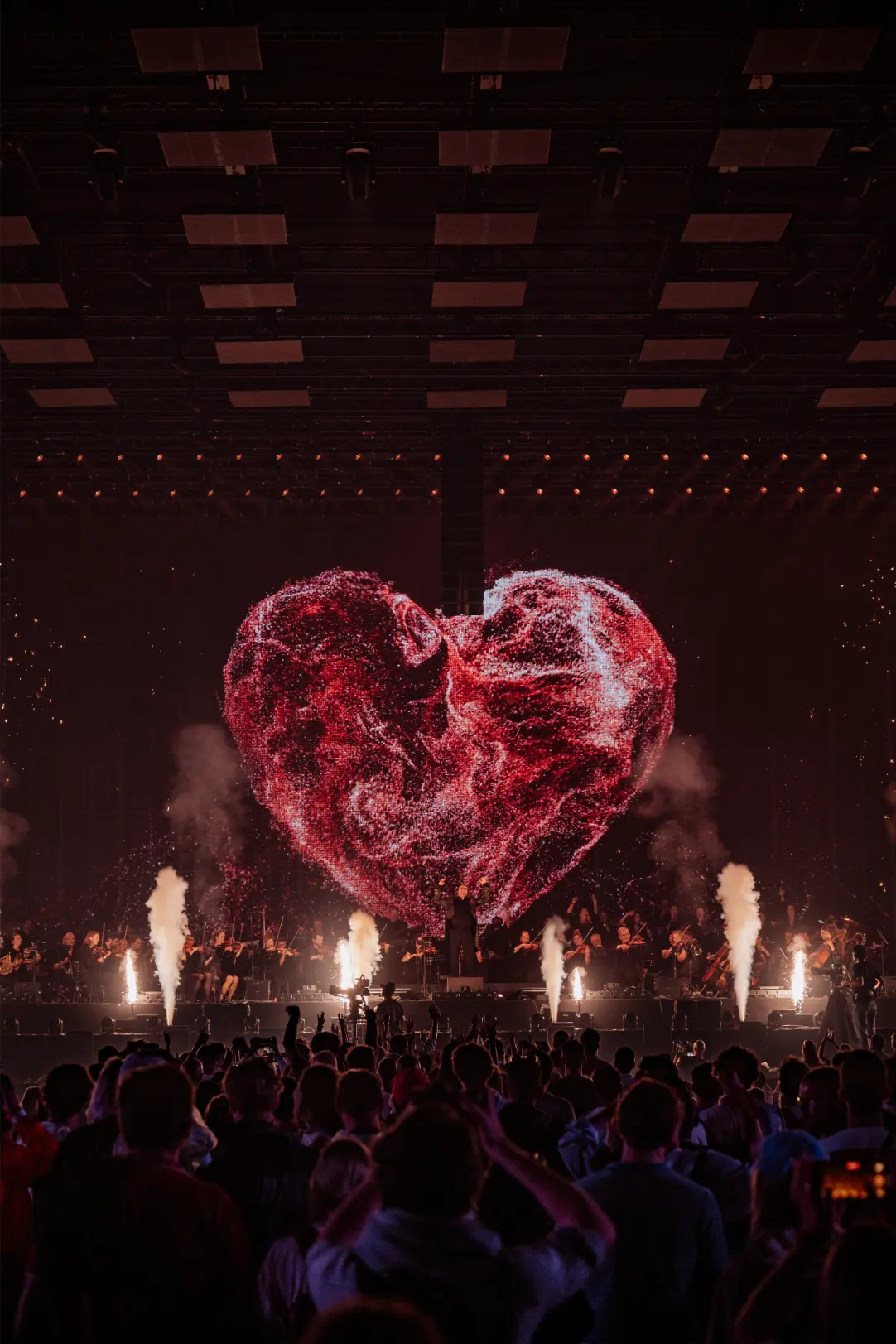 Orchestra performing on stage at the Love Tomorrow Summit with blue spotlights and the phrase 'Live Today, Love Tomorrow, Unite Forever' projected above.