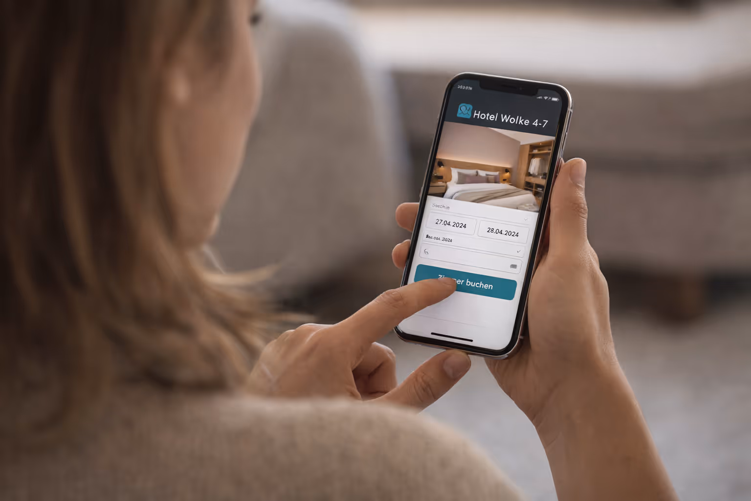 wir dehen einer Frau über die Schulter, die an ihrem Smartphone ein Zimmer im Hotel Wolke 4-7 bucht