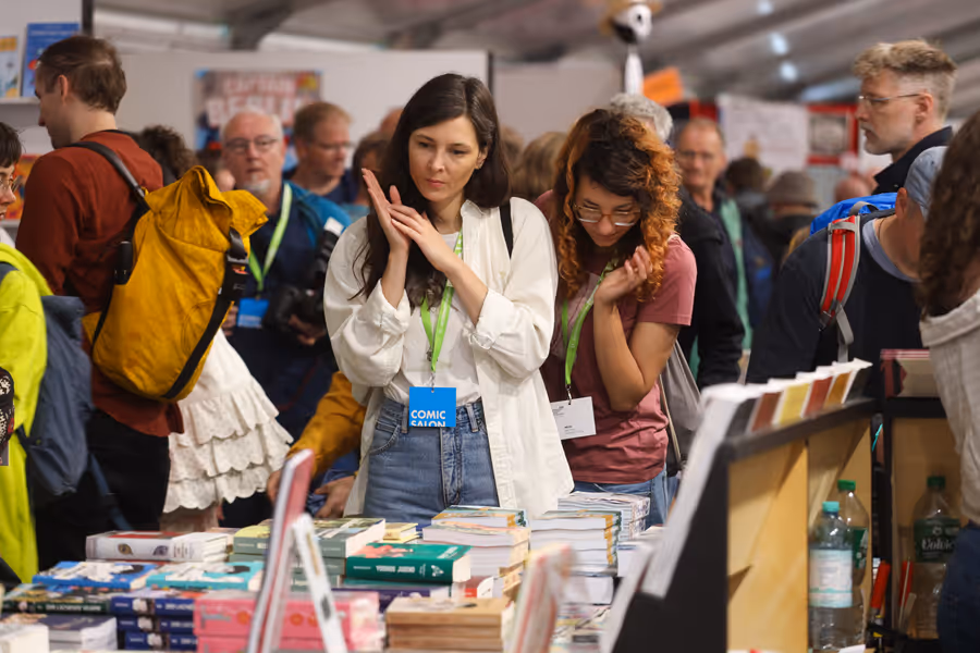 Besucher des Komic-Salon an einem langen Tisch mit Büchern und Heften