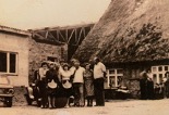 Schwarz-weiß-Foto einer Gruppe von Menschen vor einem Bauernhaus mit Reetdach.