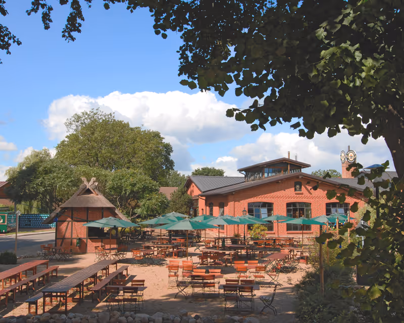 Sommerliche Idylle im Vielanker Biergarten mit Blick auf das historische Backsteingebäude der Brauerei unter strahlend blauem Himmel.