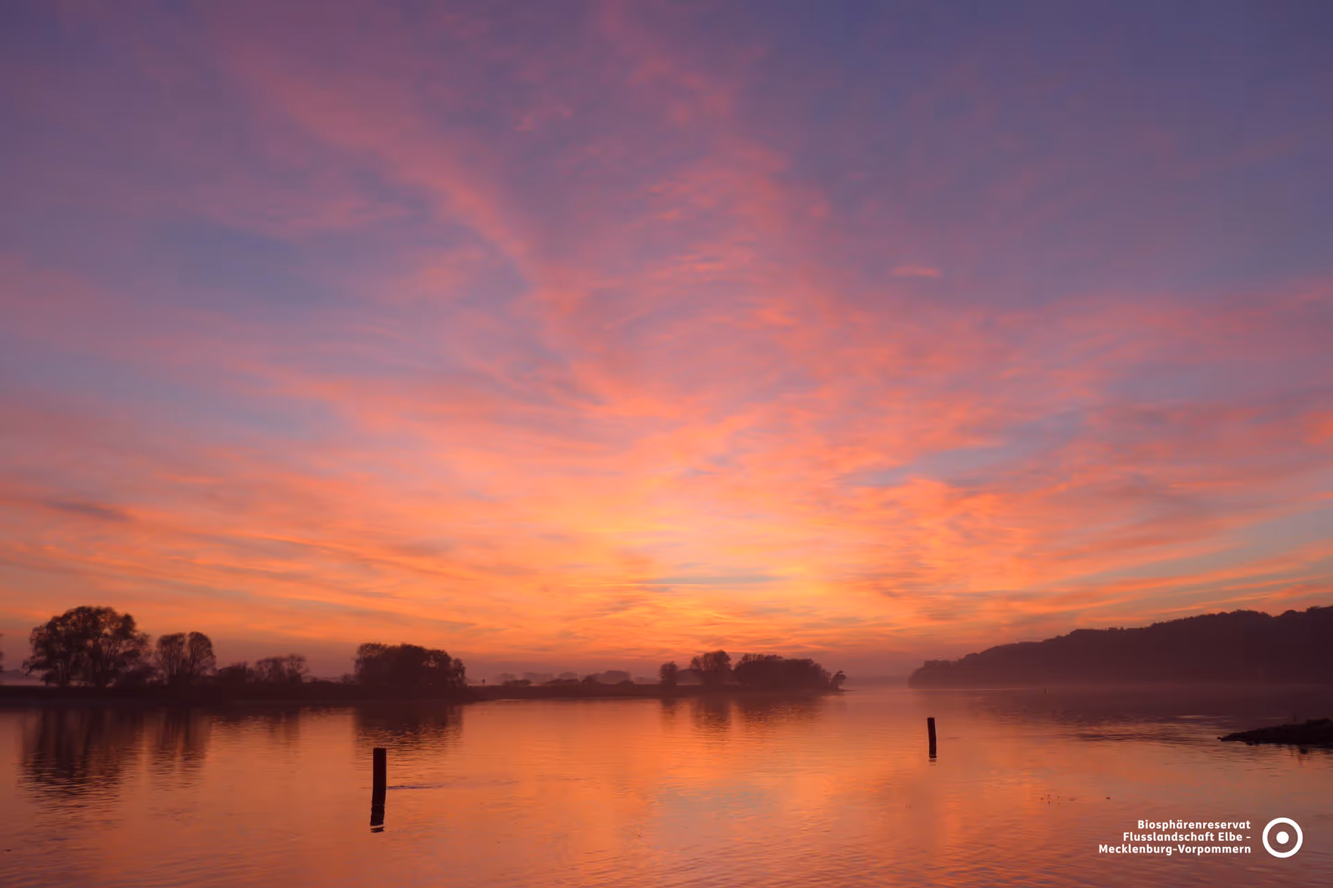 Spektakulärer Sonnenuntergang über der Elbe bei Vielank: Orange-leuchtender Himmel spiegelt sich im Wasser der Elbtalaue.