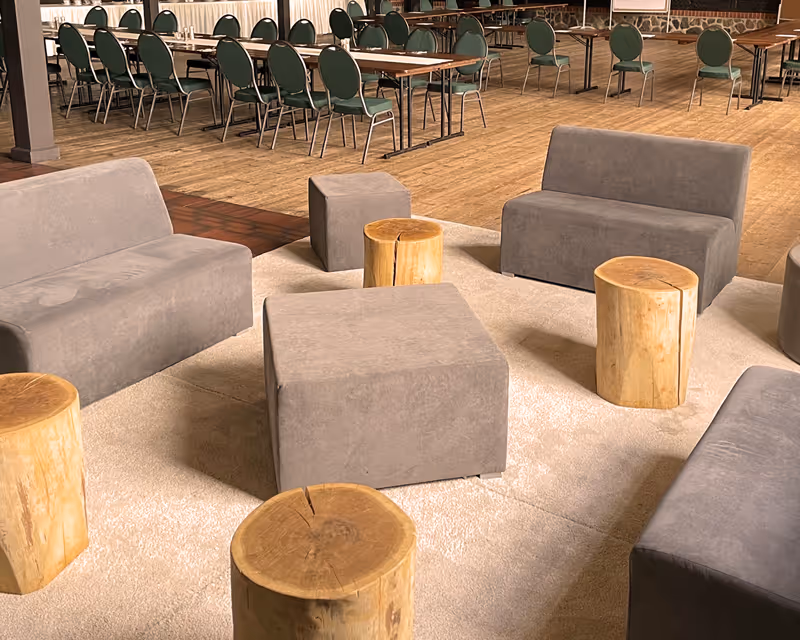 Kreative Lounge-Ecke im Vielanker Brauhaus mit modernen Polstersesseln und Natur-Stammhockern für informelle Meetings oder Pausen während einer Tagung.