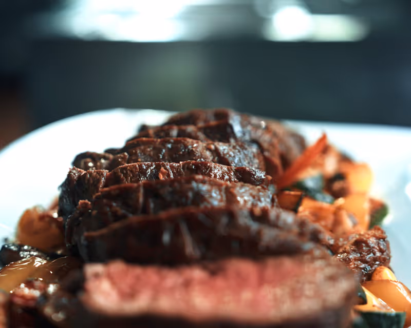 Saftiges Steak vom hauseigenen Vielanker Auerochsen, perfekt medium-rare gebraten und mit knackigem Marktgemüse auf weißem Porzellan serviert.