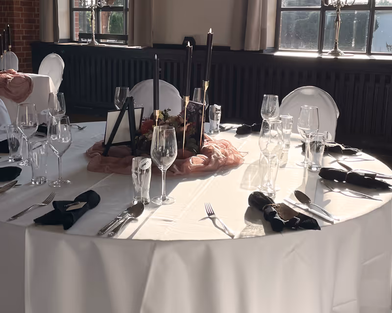 Im Vielanker Brauhaus: Elegant eingedeckter runder Tisch für eine Hochzeit oder Gala mit markanten schwarzen Akzenten, Kerzenschein und feiner Glasausstattung.