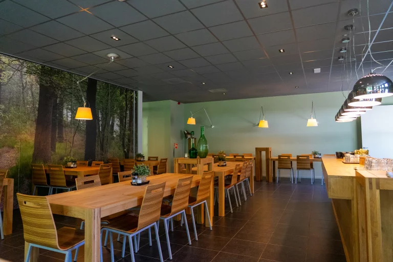 Modern eetkamer met houten tafels en stoelen, hanglampen, en een muurdecoratie met bosafbeelding.