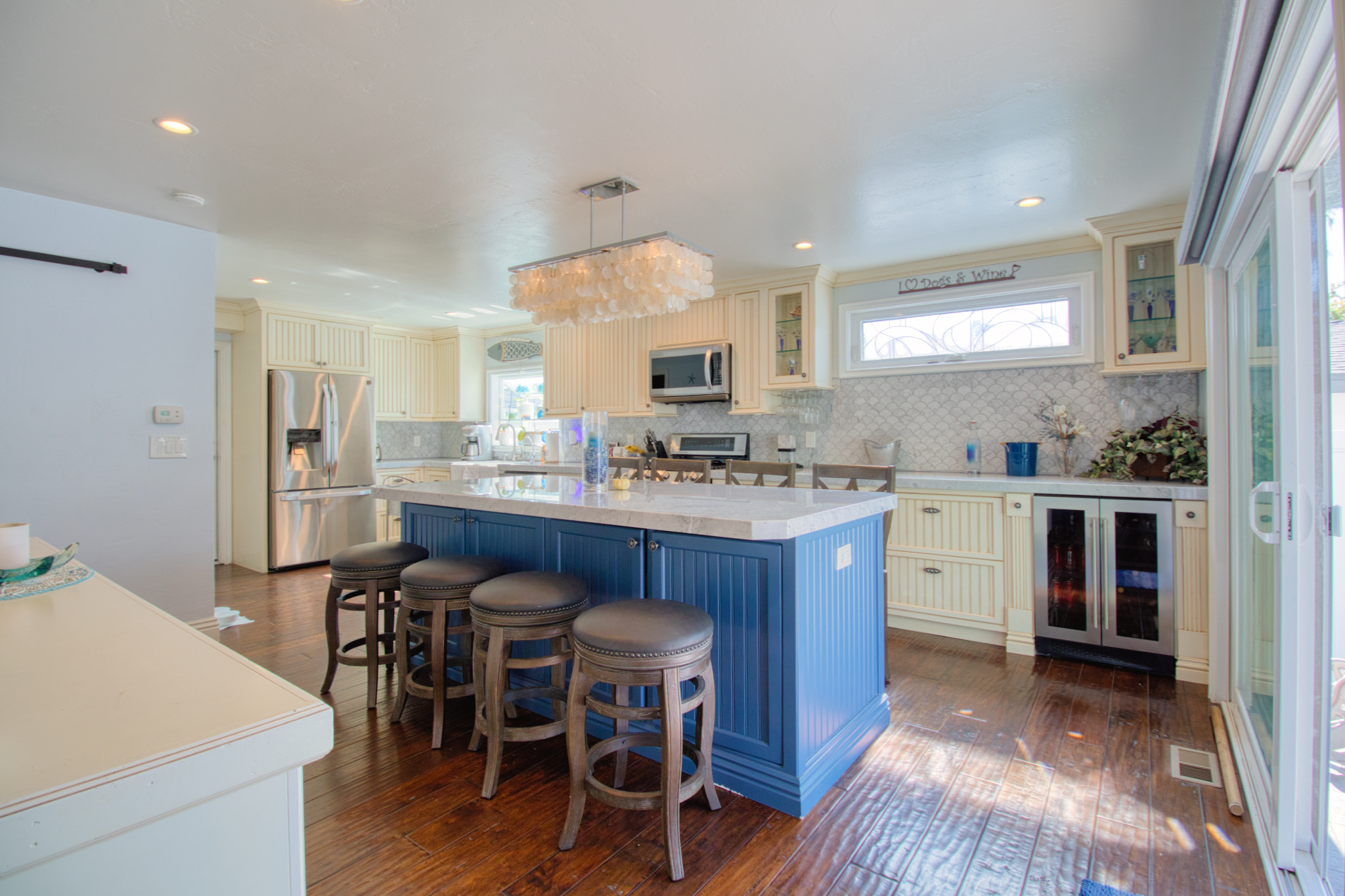 Modern kitchen with blue beadboard island, cream cabinets, white quartz counters, dark hardwood floors, and capiz shell chandelier