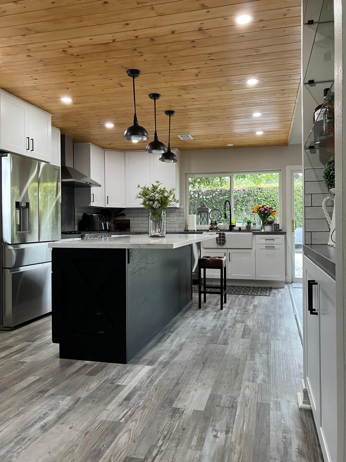 Modern farmhouse kitchen with white cabinets, dark wood island, wood plank ceiling, pendant lights, and gray luxury vinyl flooring