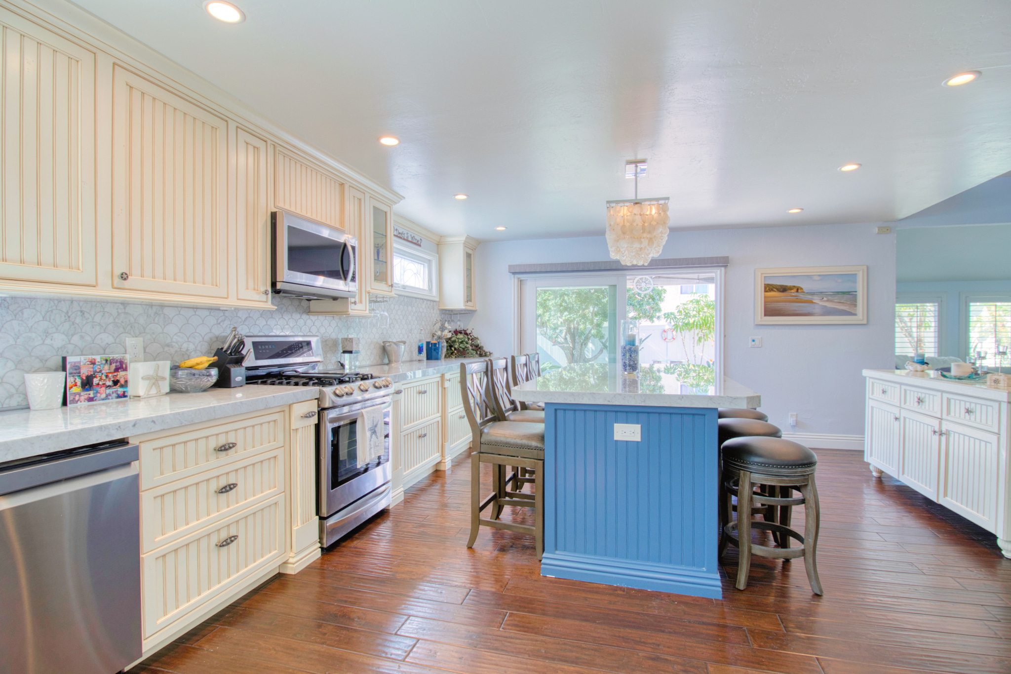 Modern coastal kitchen with cream beadboard cabinets, blue island, stainless appliances, and dark hardwood floors