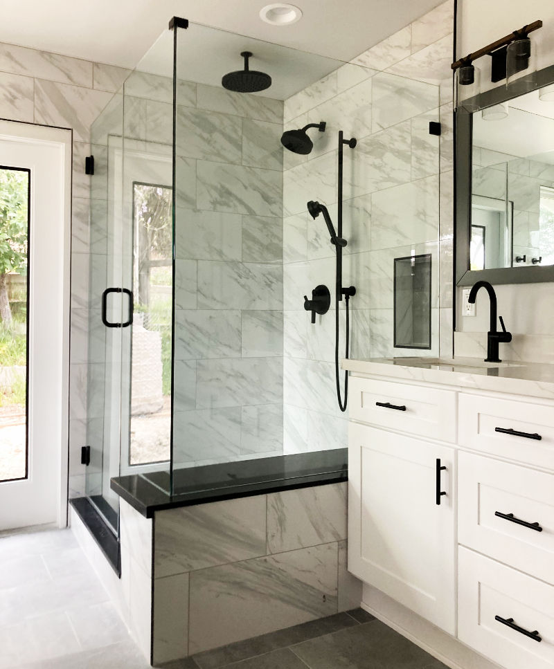Modern bathroom remodel with marble tile shower, black fixtures, white vanity cabinets, and glass shower enclosure