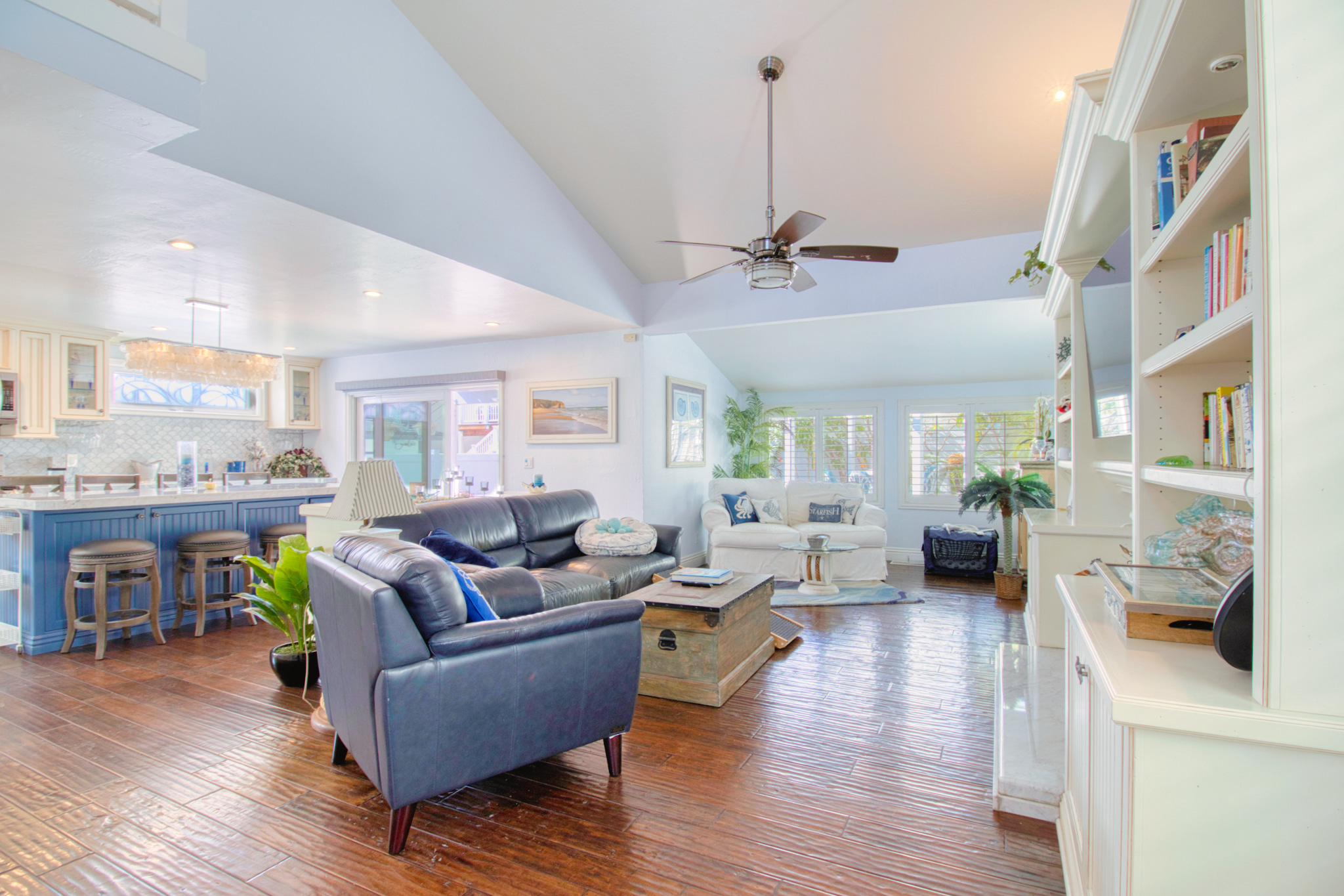 Open concept living room with dark leather sofa, wood floors, white built-in shelving, and blue kitchen island with bar stools