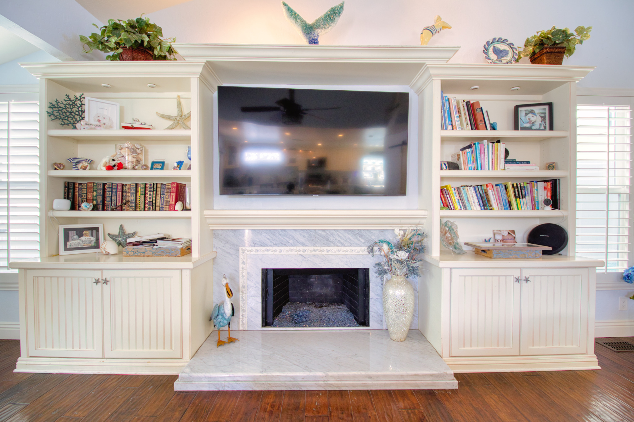 White built-in entertainment center with marble fireplace surround, open shelving displaying books and decor, mounted TV above