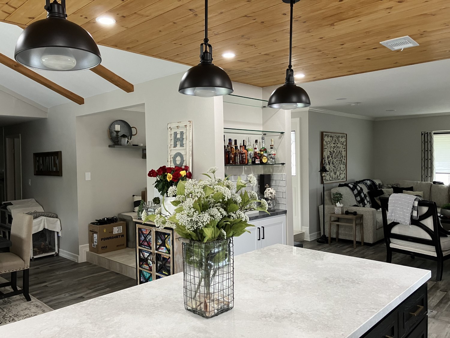 Modern farmhouse kitchen with white marble island, black pendant lights, wood beam ceiling, and open bar area