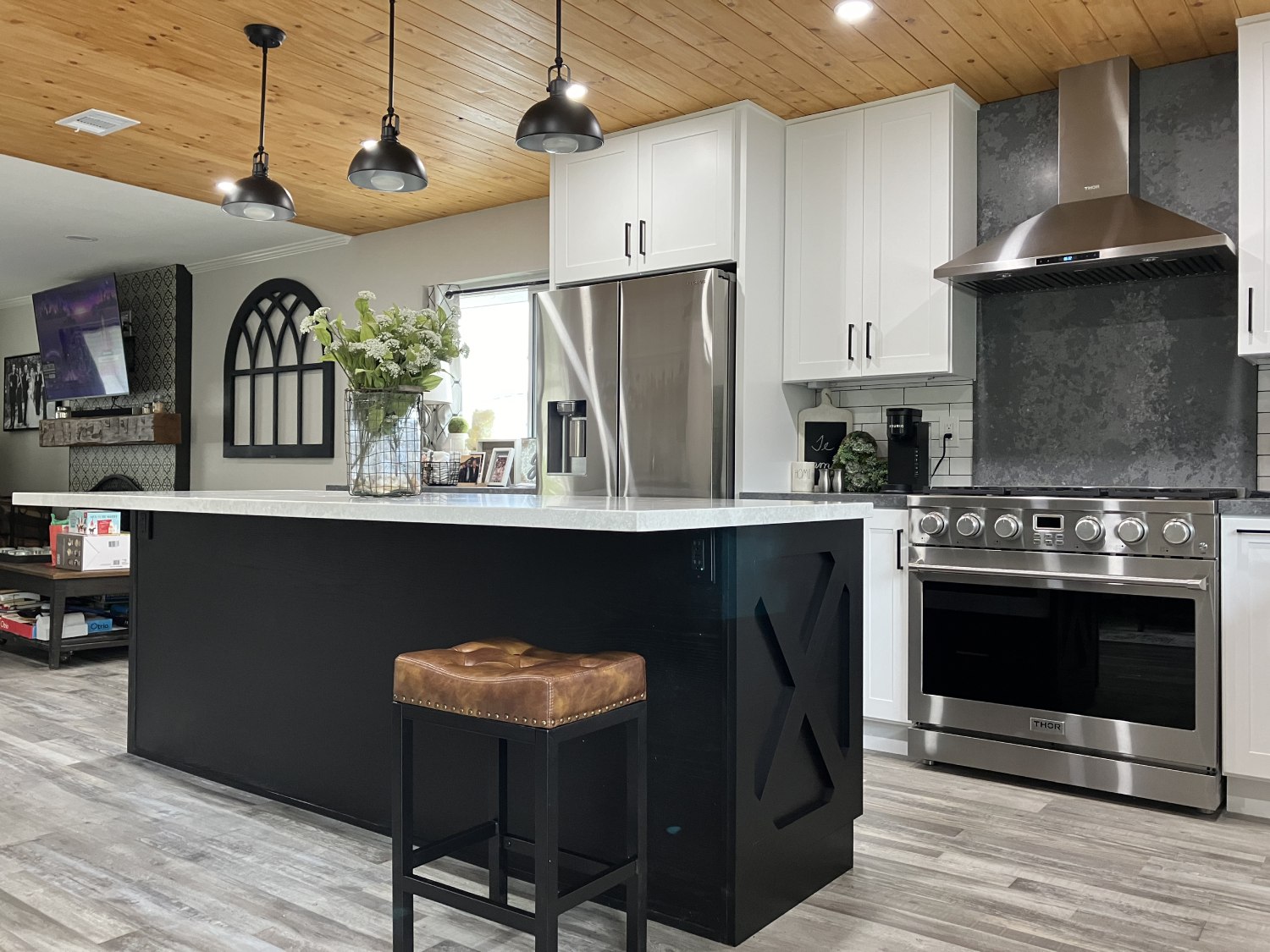Modern farmhouse kitchen with white cabinets, dark navy island, wood plank ceiling, stainless steel appliances, and pendant lights