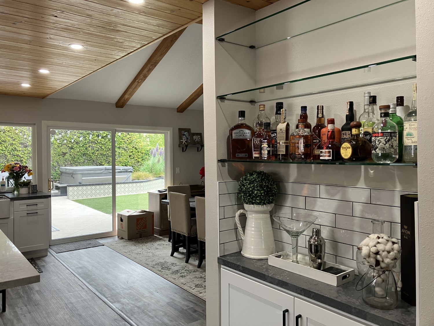 Modern farmhouse kitchen with white cabinets, gray subway tile backsplash, wood beam ceiling, and glass shelving bar area
