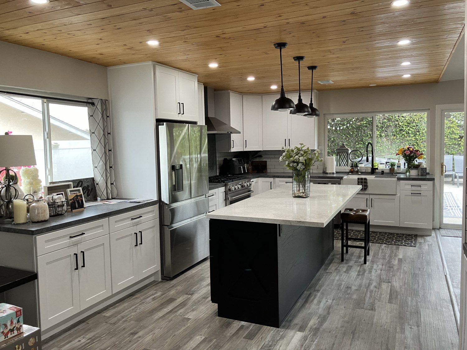 Modern farmhouse kitchen with white cabinets, dark island, wood plank ceiling, stainless appliances, and gray wood floors