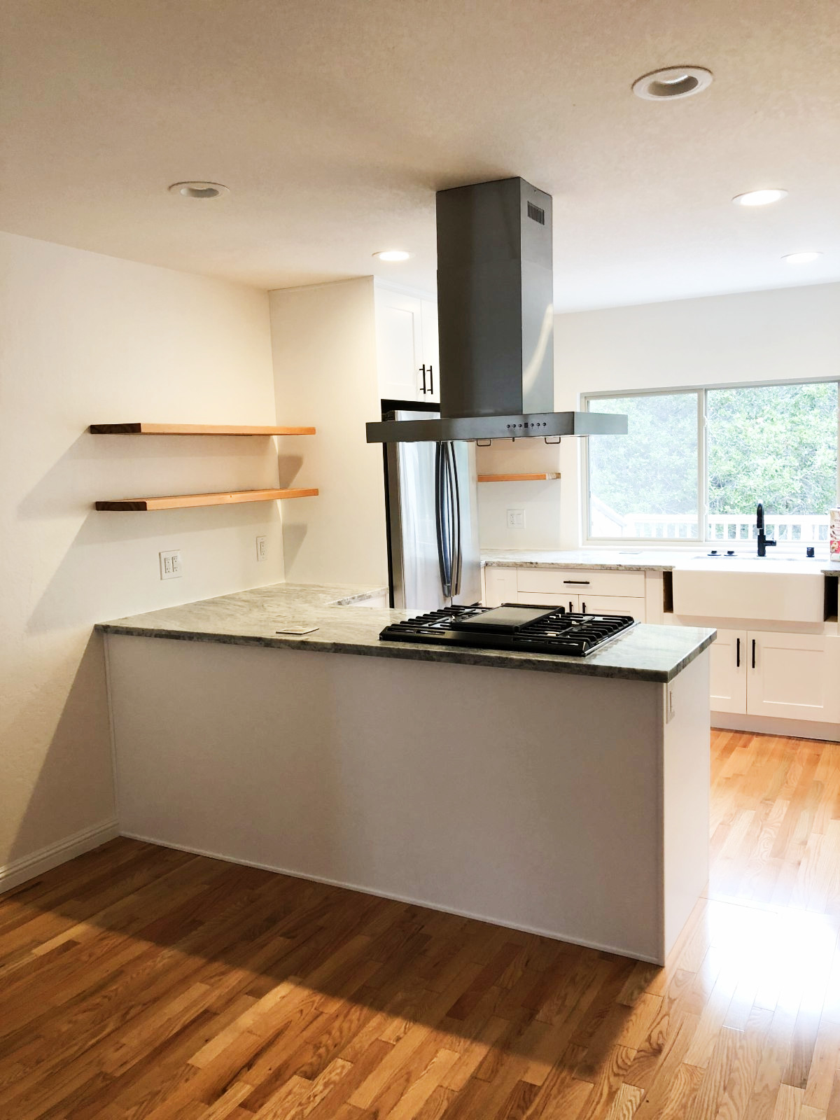 Modern white kitchen with granite countertop island, gas cooktop, stainless steel range hood, and warm wood flooring