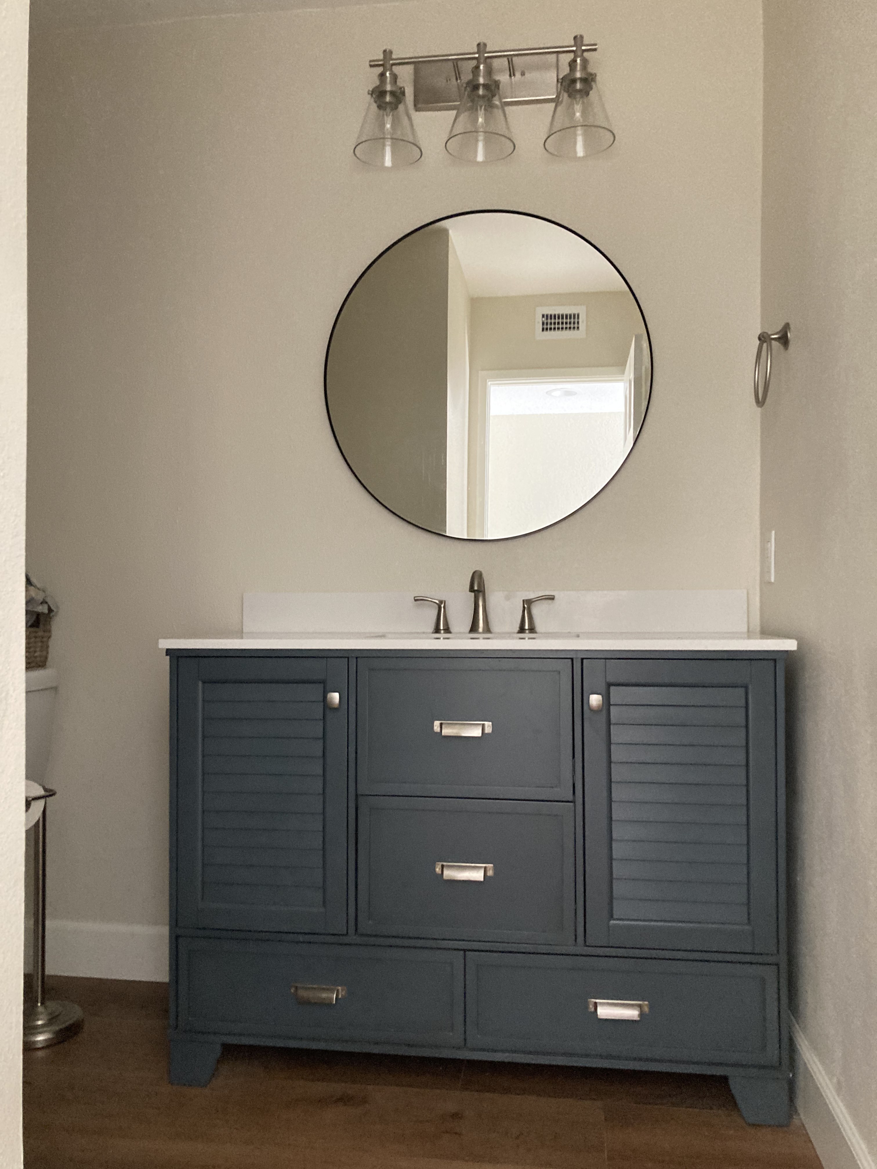 Modern bathroom vanity with dark blue shaker-style cabinets, white countertop, round black mirror, and industrial pendant lights