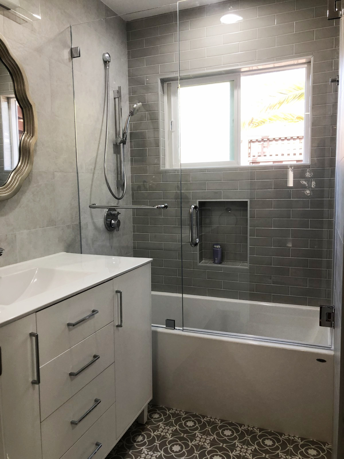Modern bathroom with gray subway tile shower, white vanity with drawers, patterned floor tile, and glass shower door