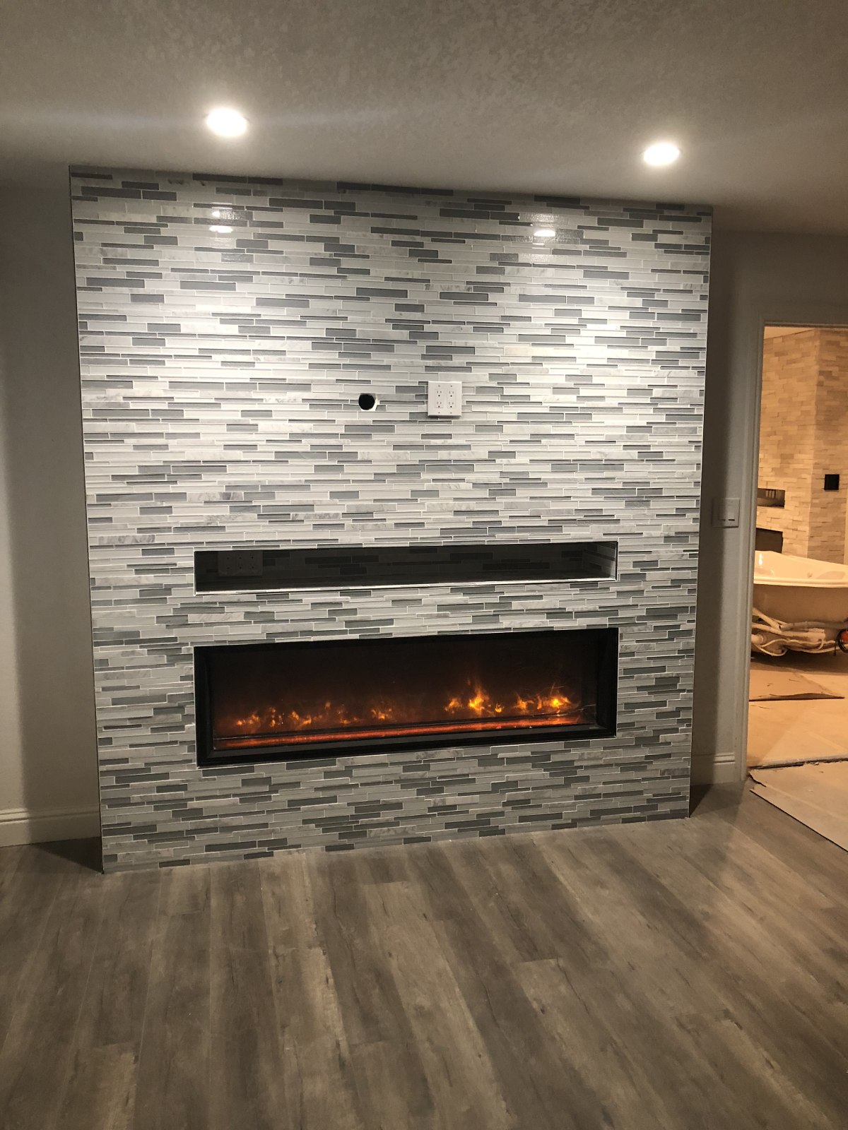 Modern linear electric fireplace with gray and white mosaic tile surround and recessed lighting in contemporary living room