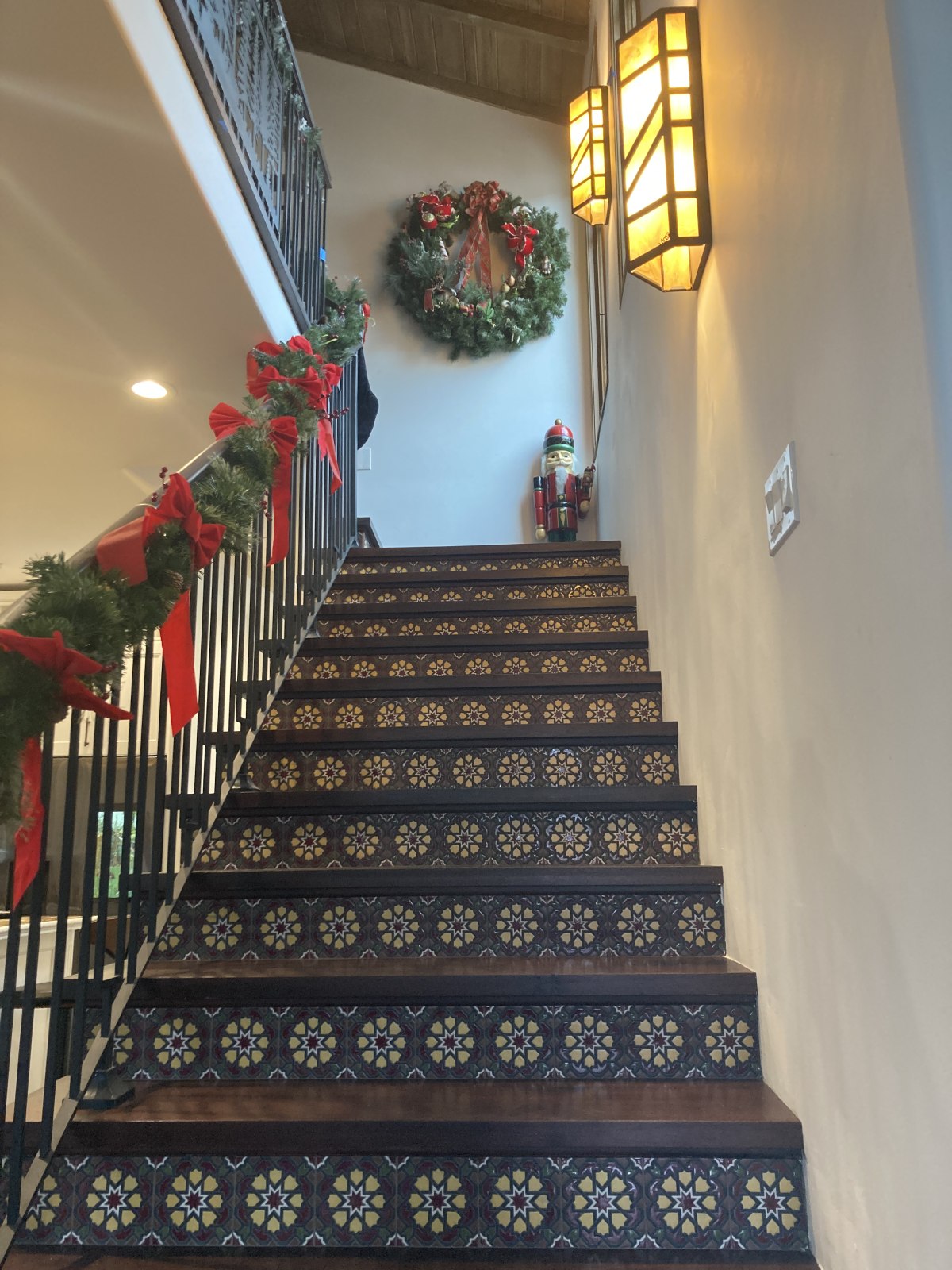 Elegant staircase with decorative tile risers, wrought iron railings, Christmas garland, and modern wall sconces