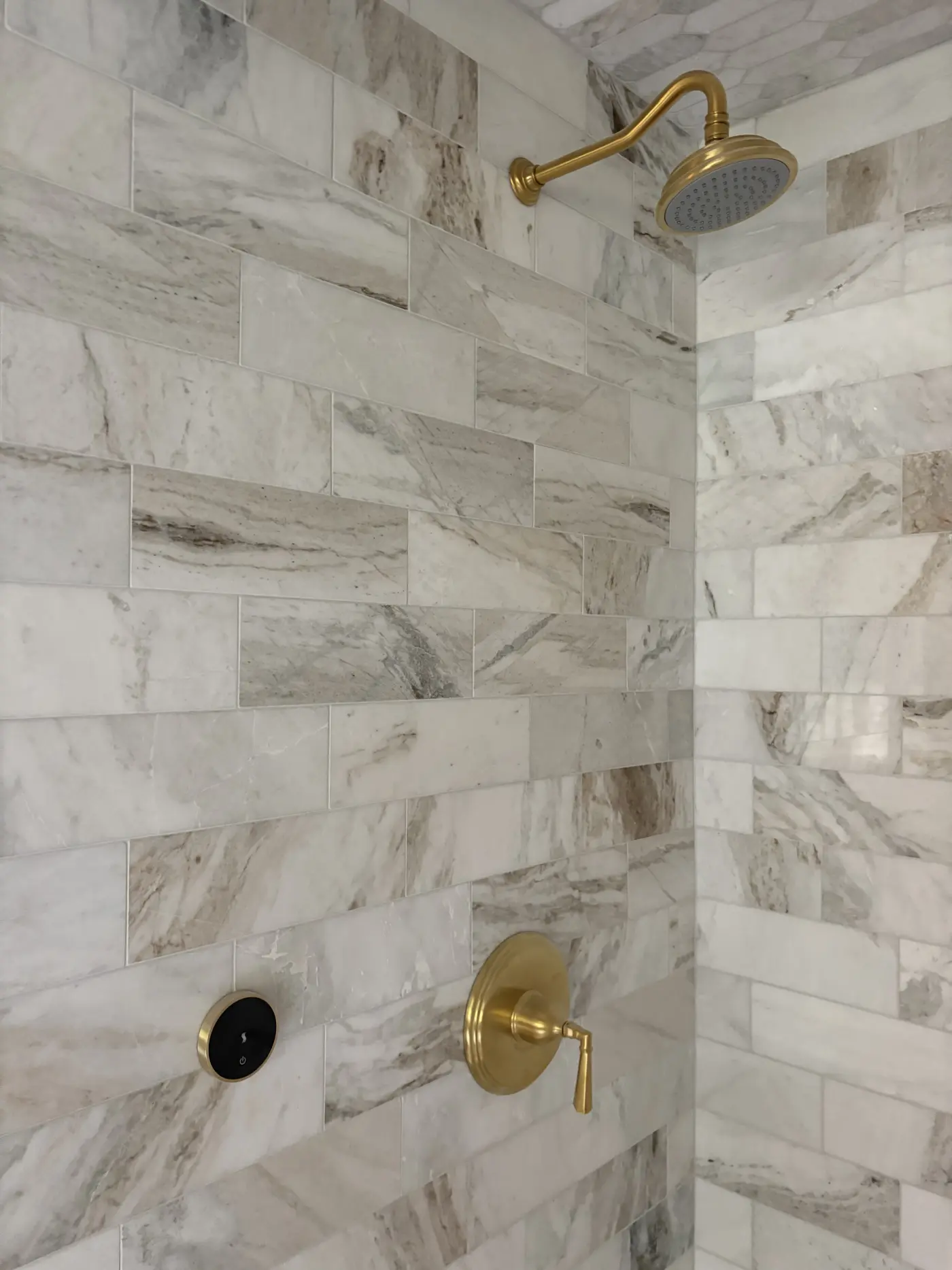 Luxury shower with white marble subway tiles and gold brass rainfall showerhead and fixtures in modern bathroom remodel