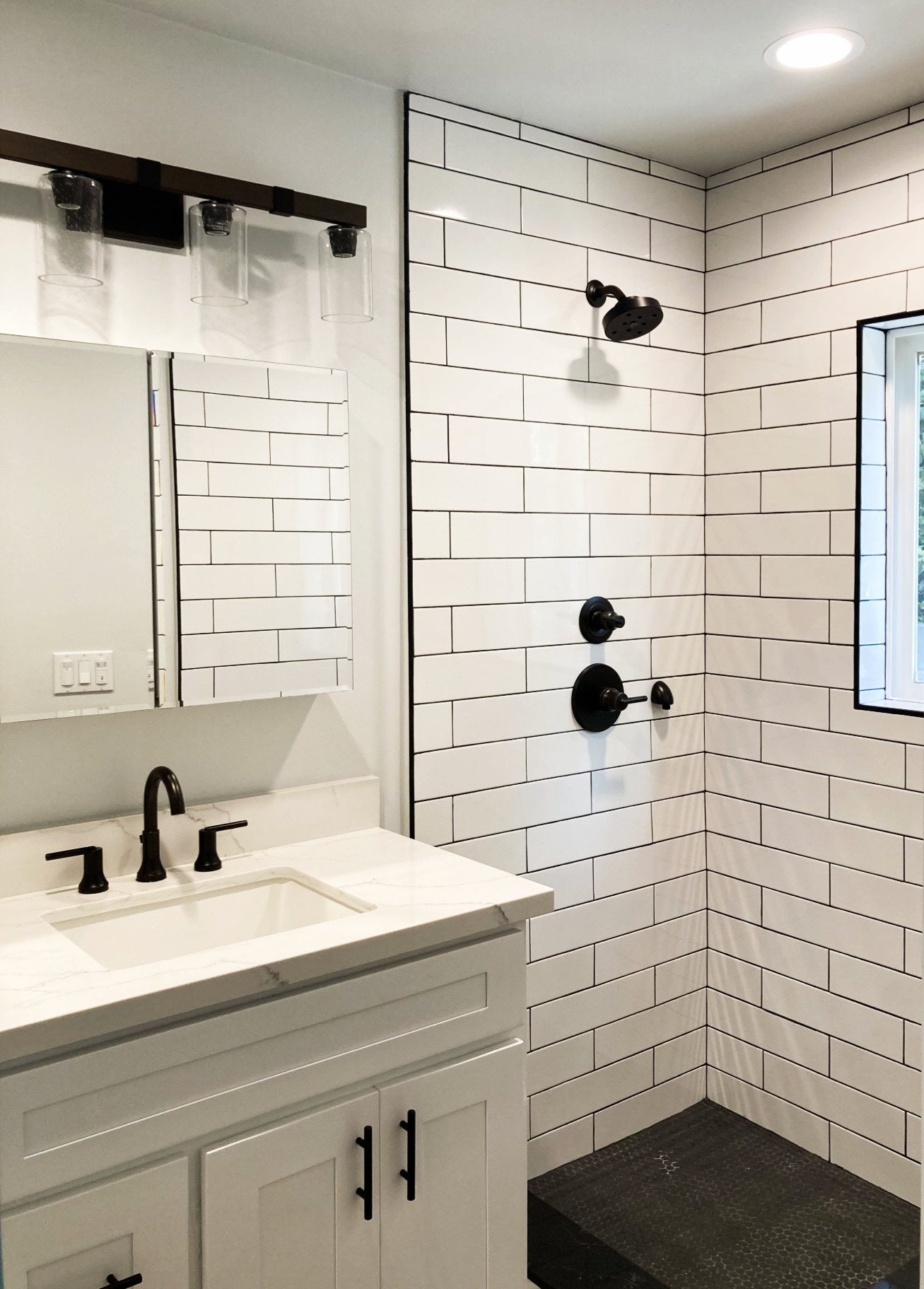 Modern bathroom with white subway tile shower, black fixtures, white vanity with black faucet, and dark speckled shower floor