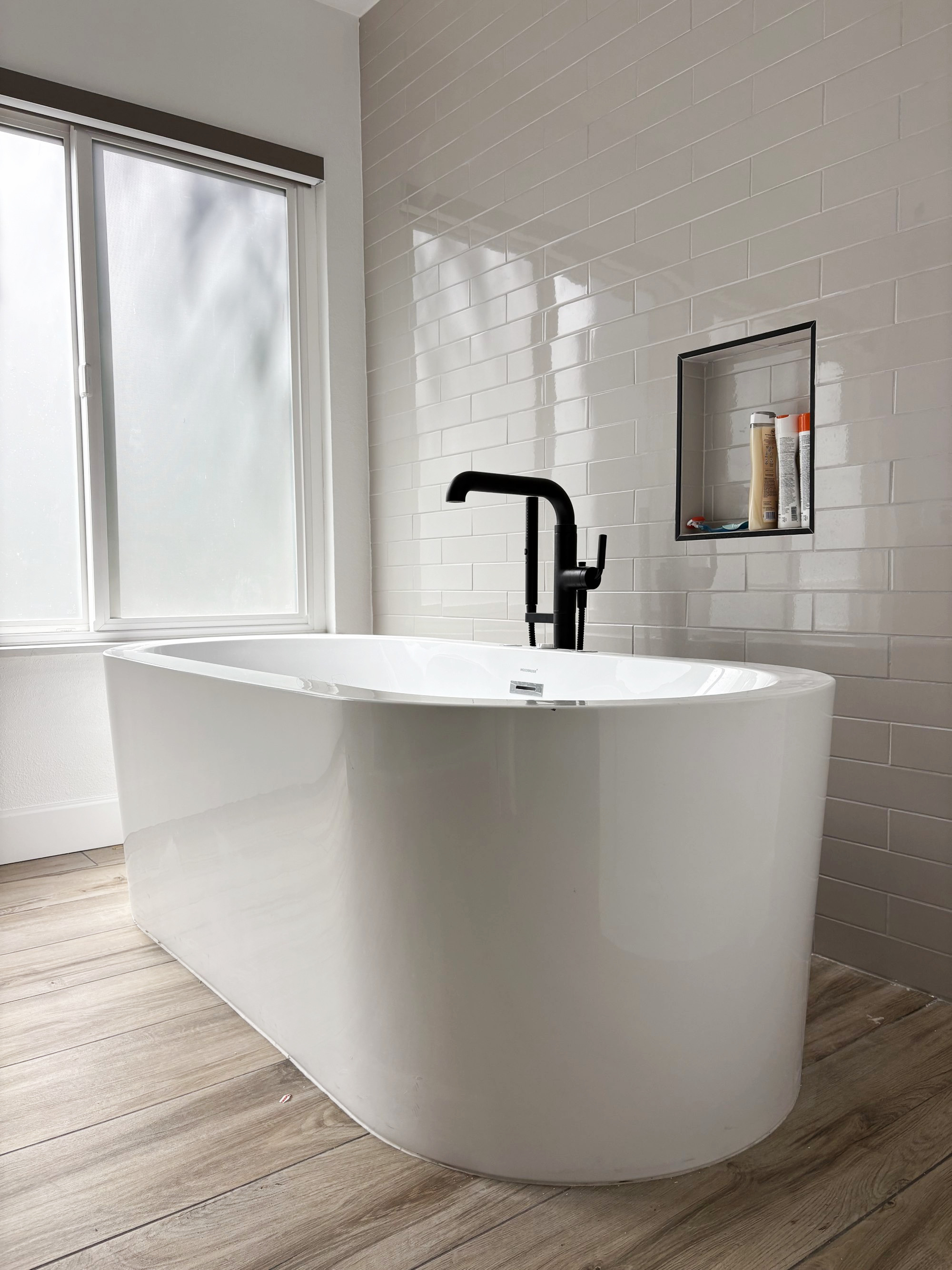 Modern bathroom with white freestanding bathtub, black faucet, white subway tile wall, and wood-look flooring