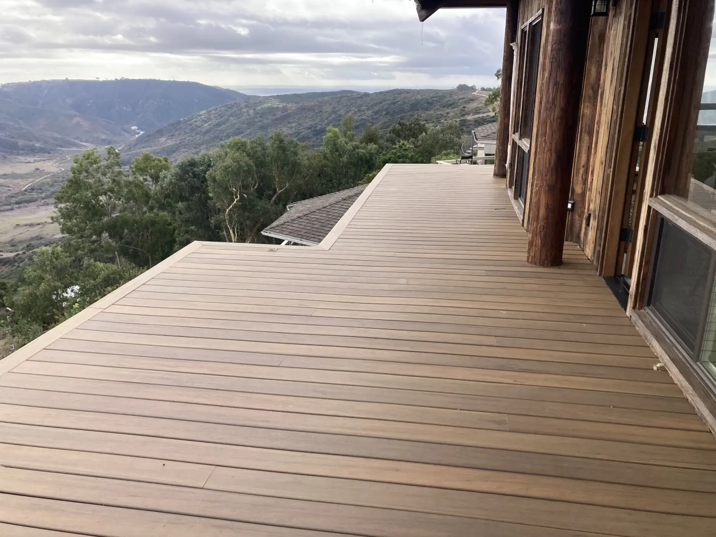 Wood deck with horizontal planking extending from modern home, overlooking rolling hills and green valleys in Orange County