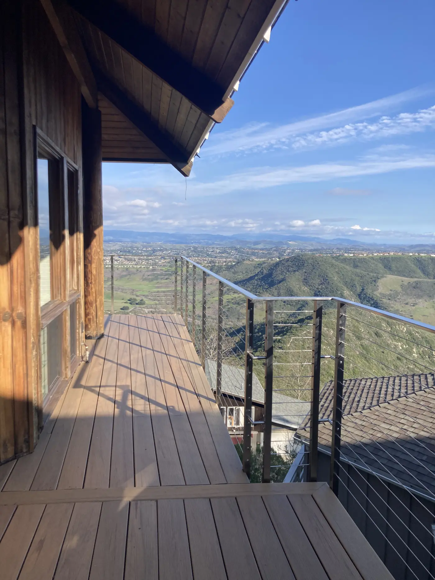 Modern hillside deck with natural wood planking, cable railing, and panoramic mountain valley views in Orange County