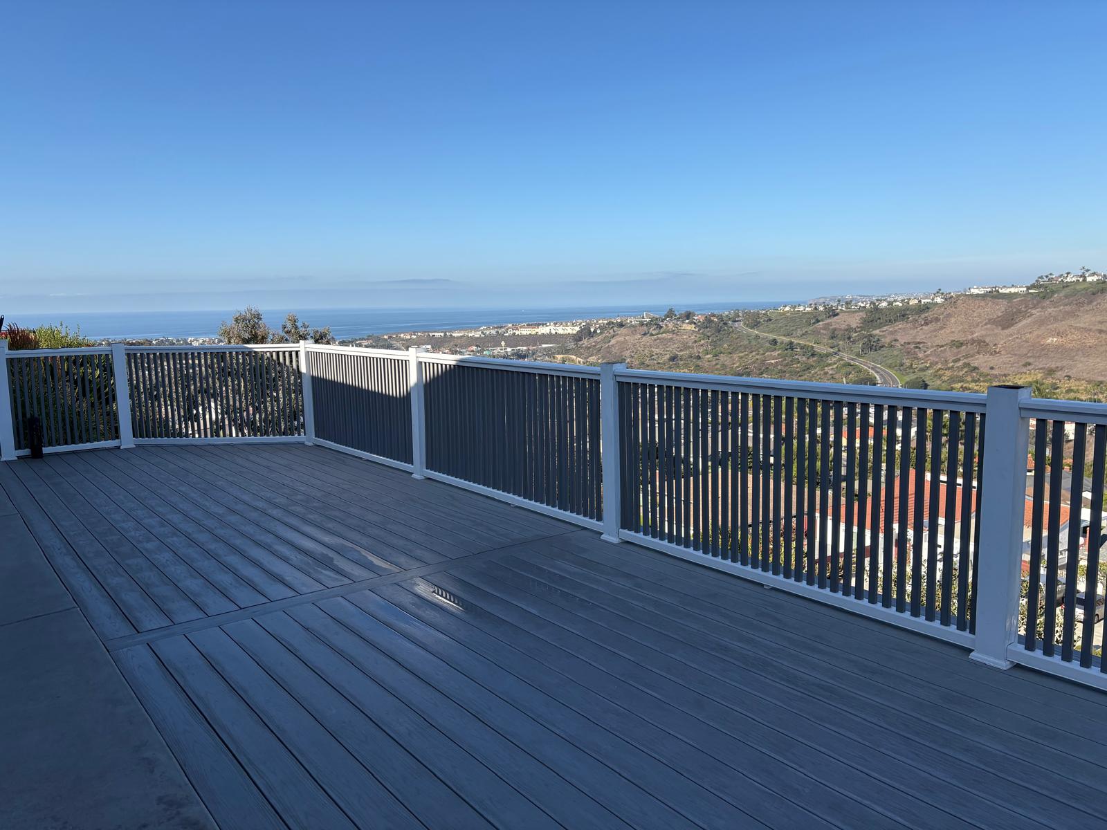 Modern gray composite deck with white railing and black vertical balusters overlooking coastal hills and ocean view