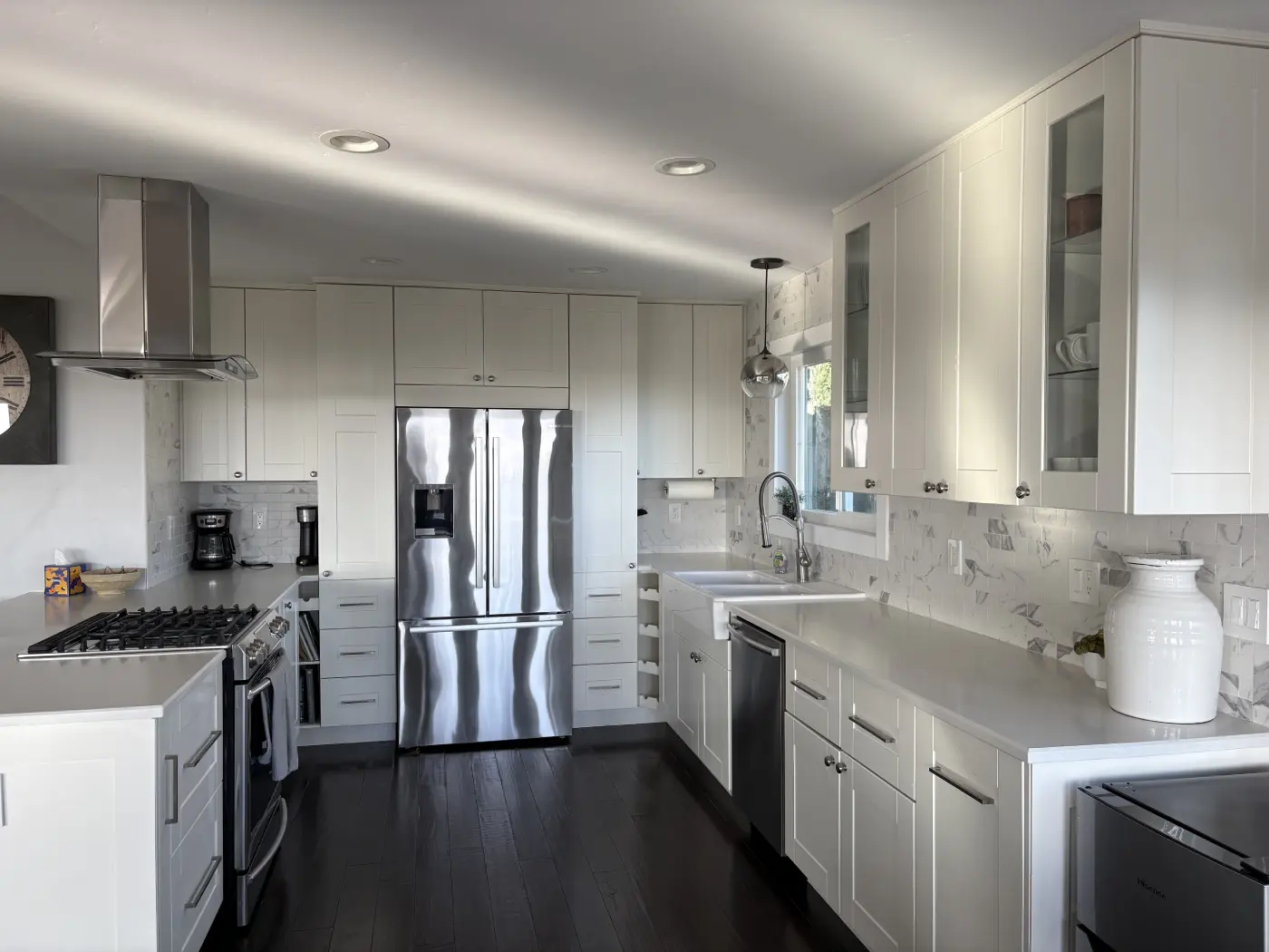 Modern white kitchen with marble backsplash, stainless steel appliances, dark hardwood floors, and quartz countertops