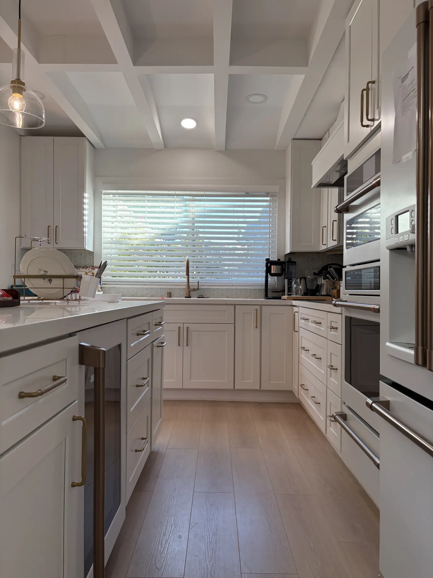 Modern white galley kitchen with shaker cabinets, quartz countertops, stainless steel appliances, and coffered ceiling