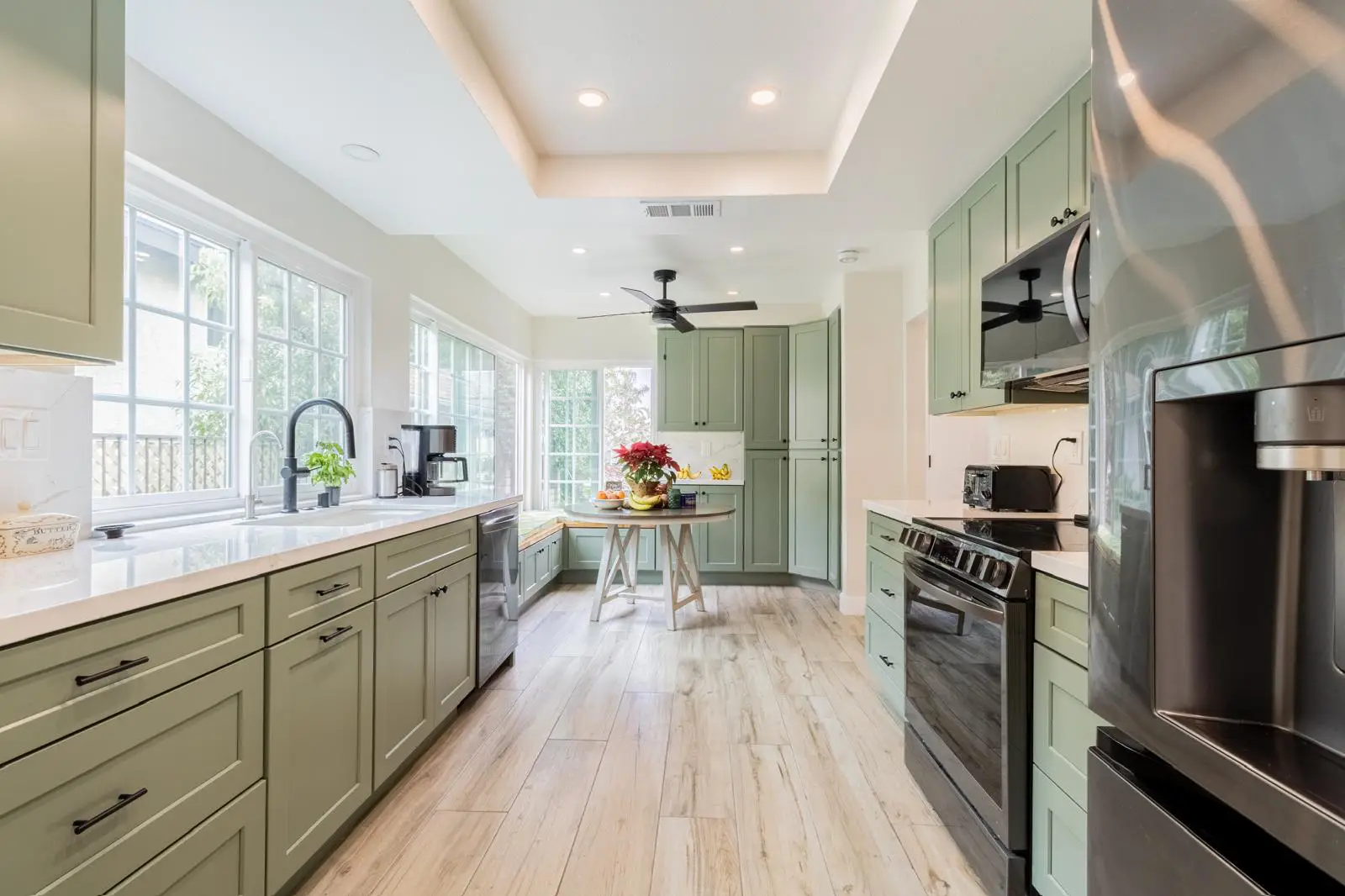 Modern kitchen with sage green cabinets, white quartz countertops, stainless steel appliances, and light wood floors