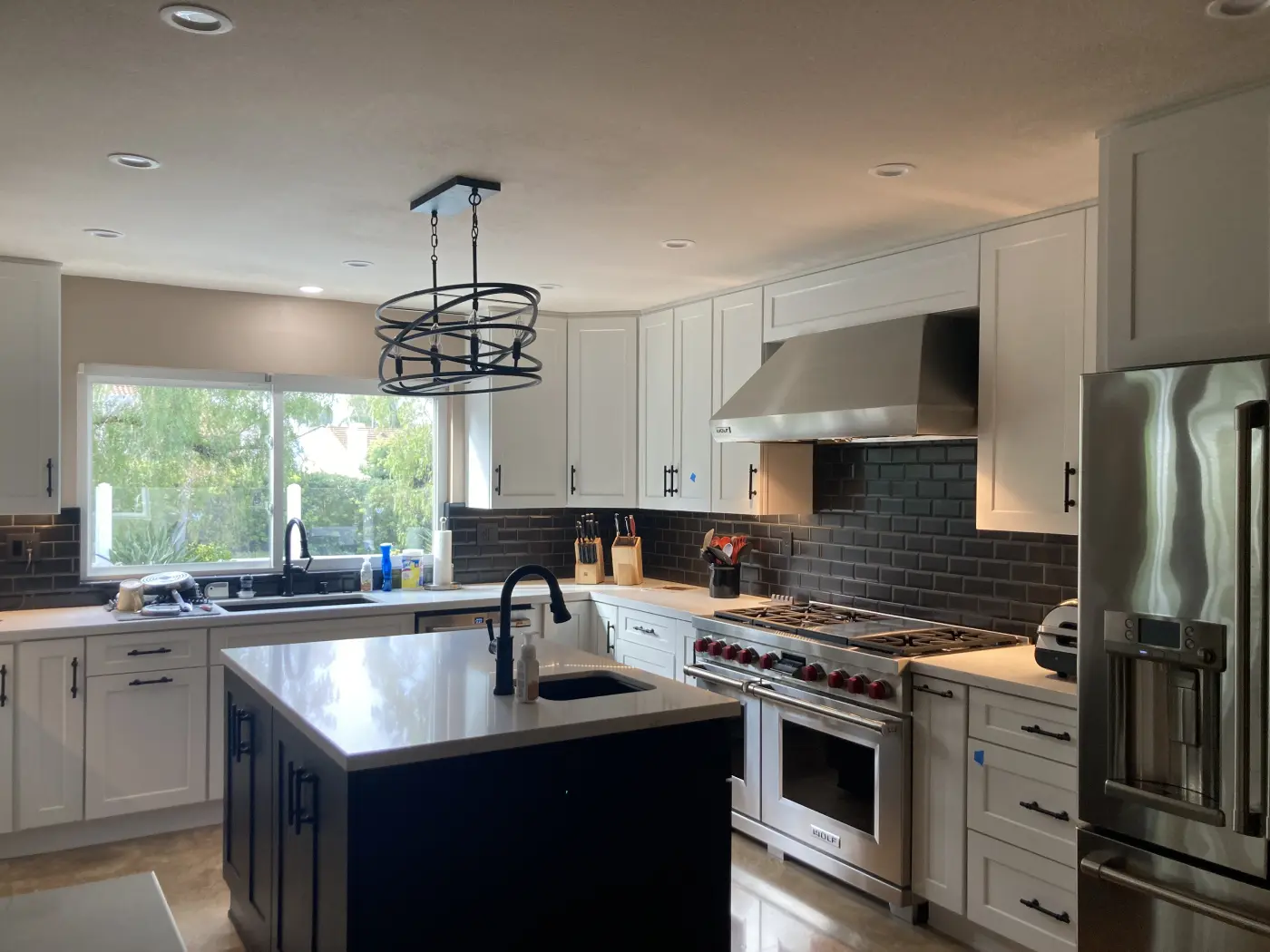 Modern white kitchen with dark subway tile backsplash, black island, stainless steel appliances, and circular pendant lighting