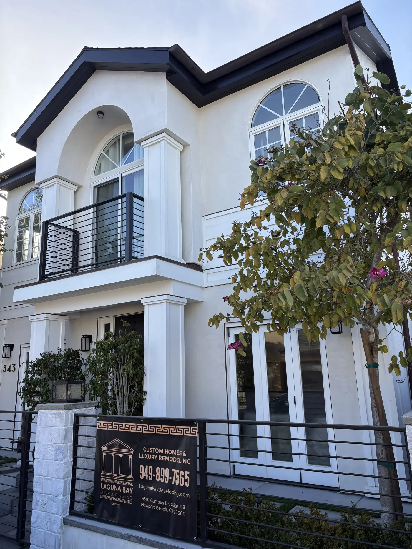 Modern two-story white stucco home with black trim, arched windows, second-floor balcony with black railings, and front columns