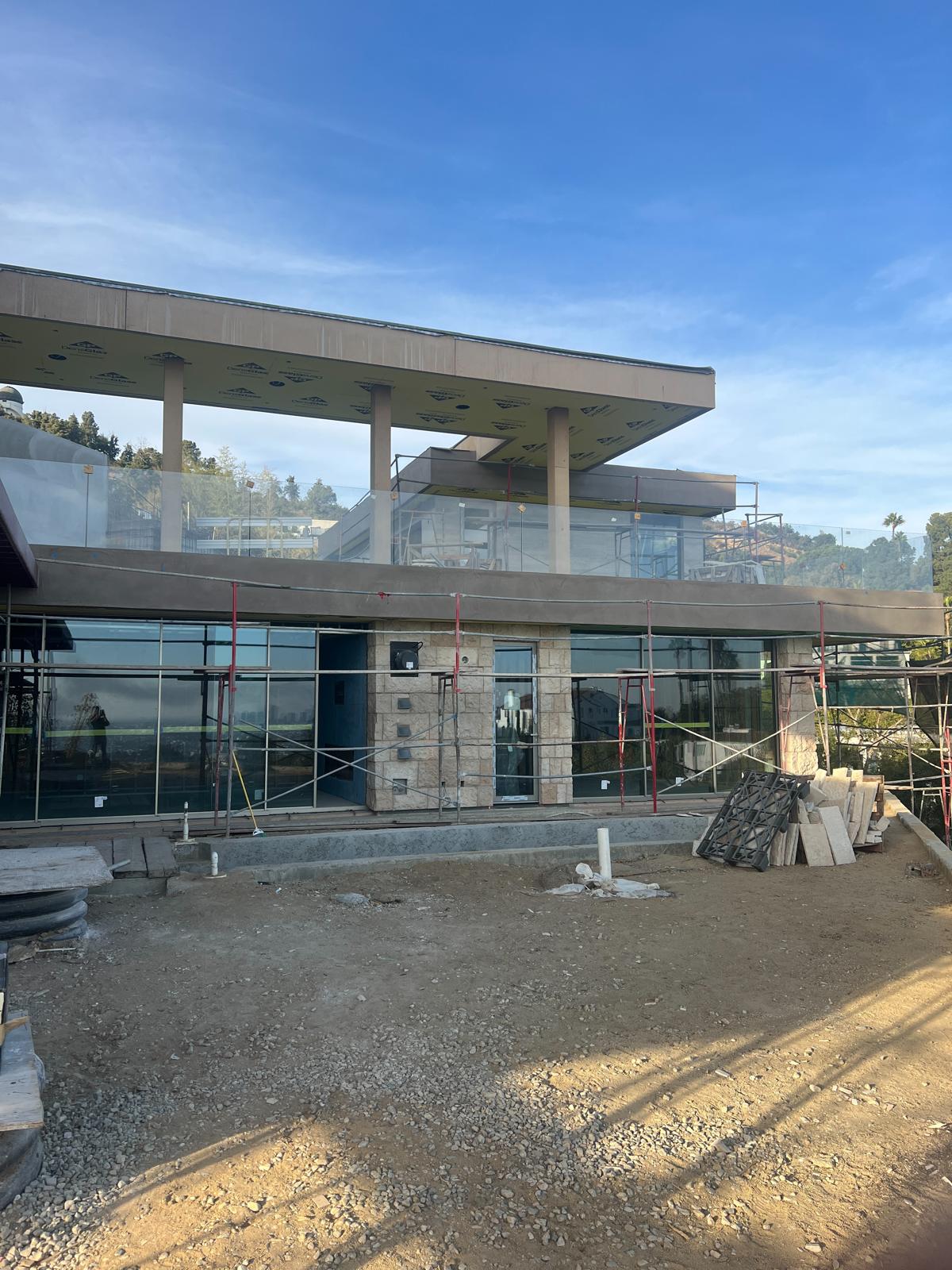 Modern glass and concrete home under construction with scaffolding, featuring large windows and contemporary architectural design