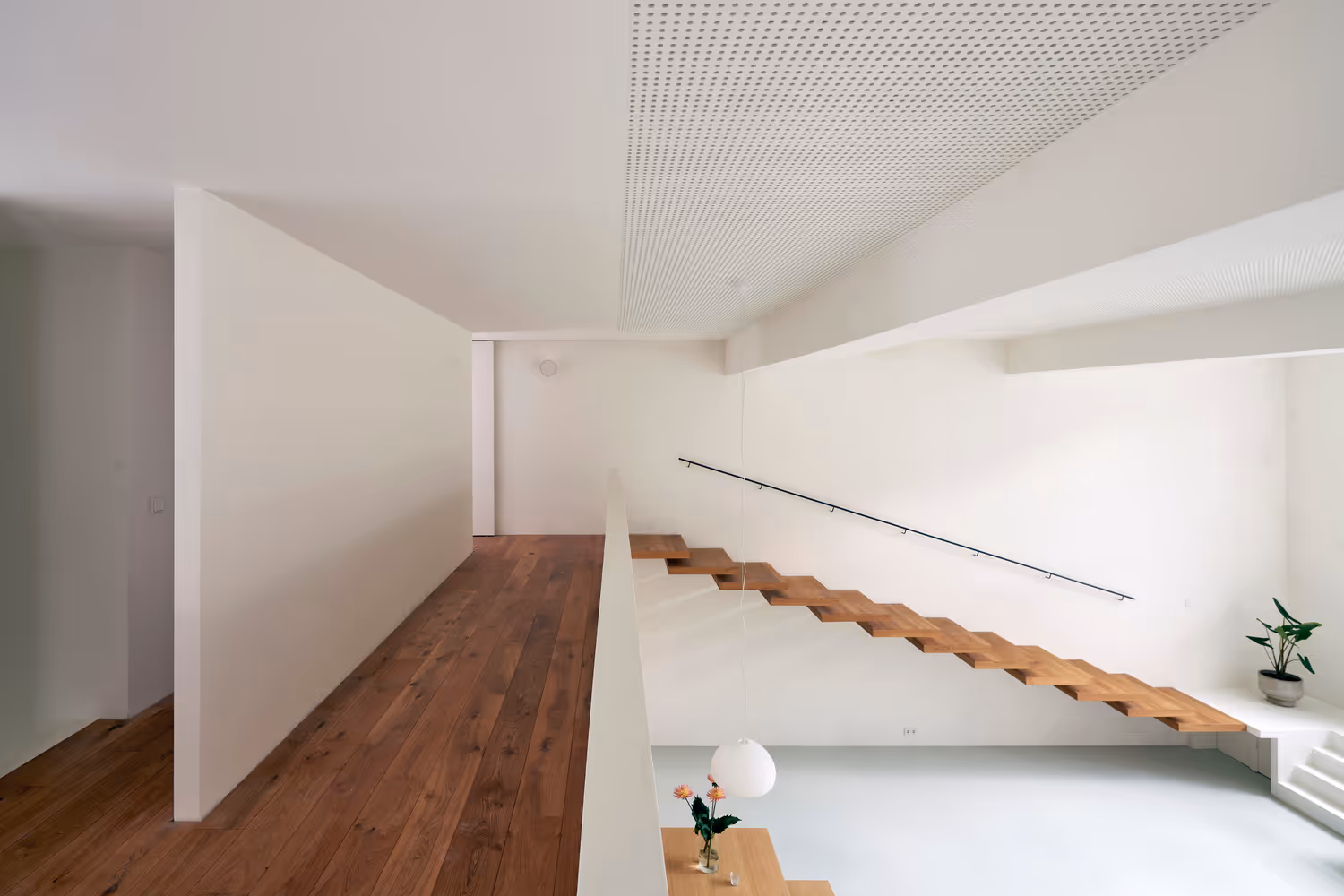 Minimalist interior with floating wooden staircase, white walls, wooden floor, and a plant in the corner.