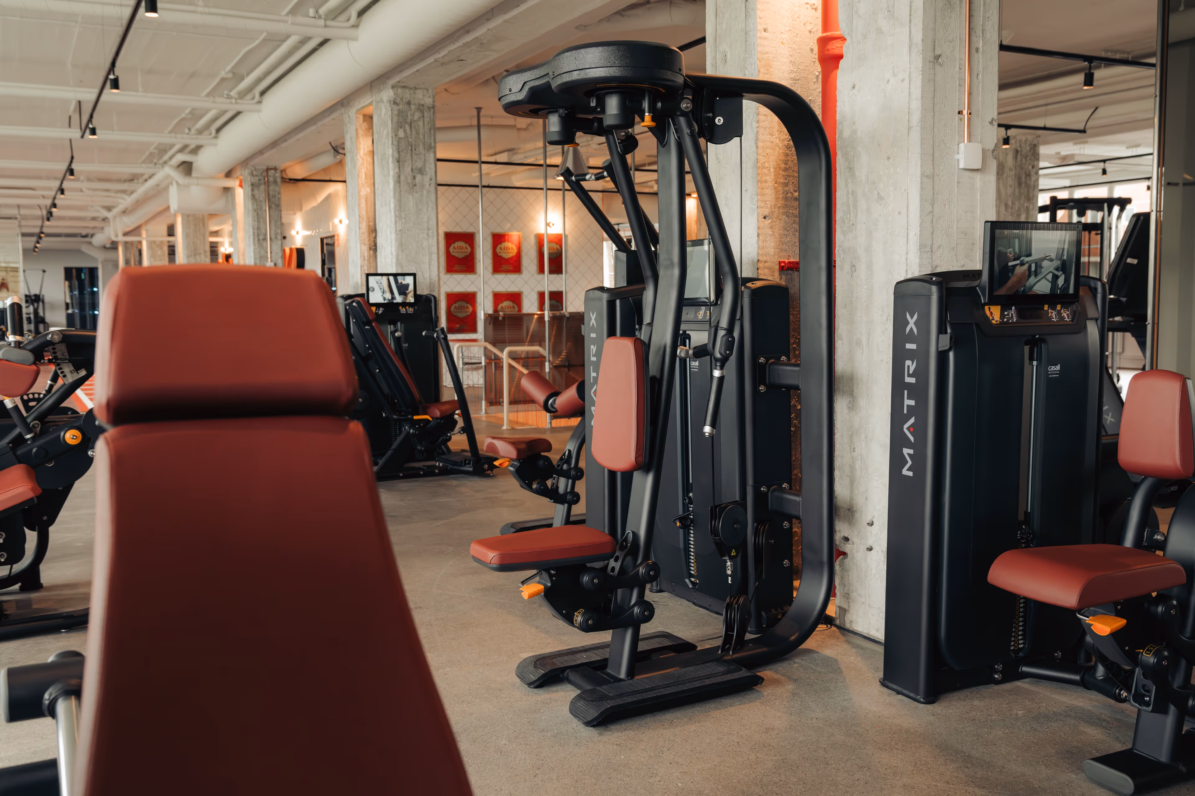Modern gym interior with black and maroon Matrix strength-training machines including chest press and leg exercises.