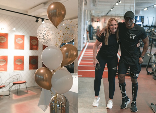 A cluster of metallic and white balloons indoors next to two smiling fitness trainers posing together in a gym.