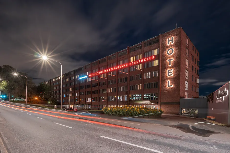 Night view of a large brick hotel building with illuminated 'HOTEL' sign and red neon signs for conference, restaurant, and health club.